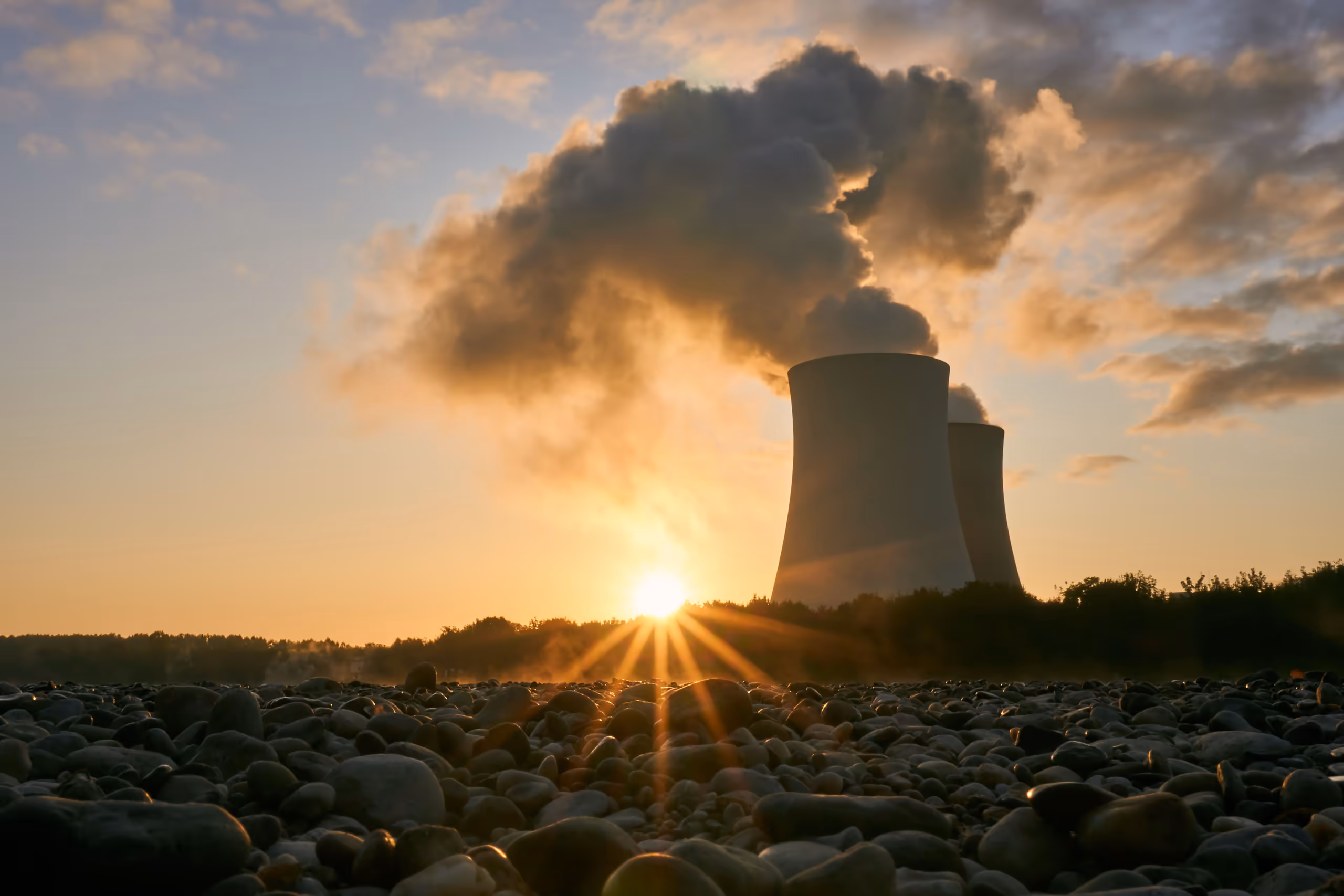 Nuclear power station cooling towers emitting steam, silhouetted against a sunrise